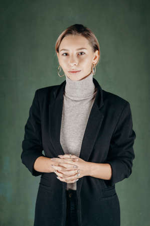 Woman in gray golf and black jacket standing against dirty green backgroundの写真素材