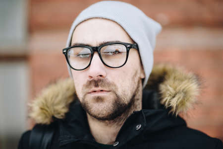 Profile of attractive happy young man with beard standing in winter city. Glasses, jacket, hat, bagpack. Color.の写真素材