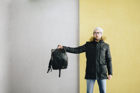 Profile of attractive happy young man with beard standing in winter urban. Gray yellow wall....