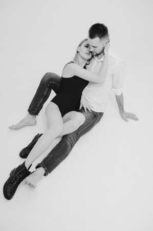 Monochrome portrait. Lovely young couple in studio. Man wearing in denim clothes and leather jacket. Beautiful young sexy girl in black bodysuit and shoes.の写真素材