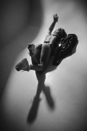 Blond girl with glamor figure posing on white dark background in lingerie. Portrait of stylish seductive girl underwear in the dark room. Low key photo with film gain.の写真素材