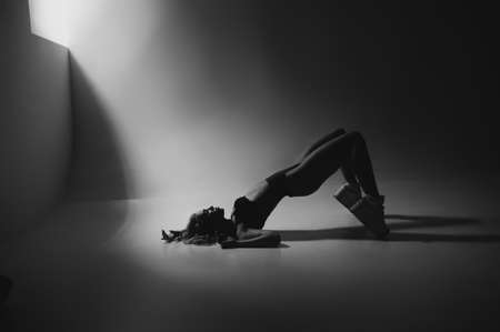 Blond girl with glamor hairstyle posing on white dark background in lingerie. Portrait of stylish seductive girl underwear in the dark room. Low key photo with film gain.の写真素材
