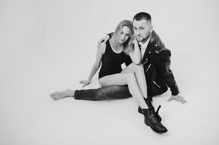 Monochrome portrait. Lovely young couple in studio. Man wearing in denim clothes and leather jacket....