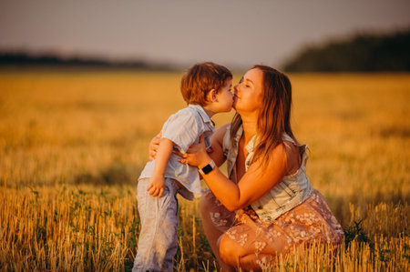 Cute cheerful child son with mother in field at sunset on a summer day. Family conceptの写真素材