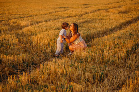 Cute cheerful child son with mother in field at sunset on a summer day. Family conceptの写真素材
