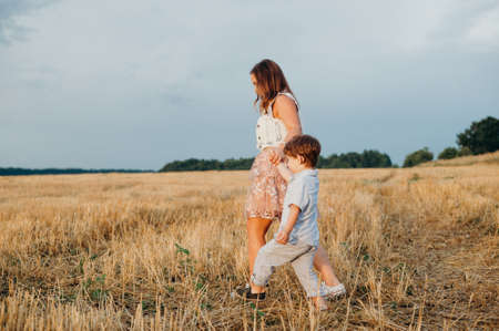 Cute cheerful child son with mother in field at sunset on a summer day. Family conceptの写真素材
