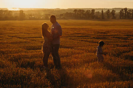 The concept of a happy family. Son with mom and daddy. Happy family in the field evening light of a sun. Mother, father and baby son happy walk at sunset, parents hold the baby.の写真素材