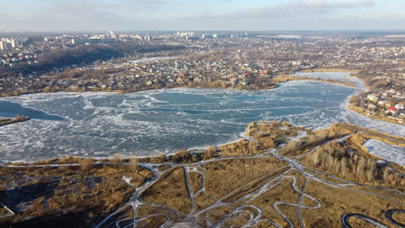 Cracks on the surface of the blue ice. Frozen lake in citys. Winter aerial cityscape of town with lake. It is snowing. Splendid morning view from dron. Traveling concept background.の写真素材