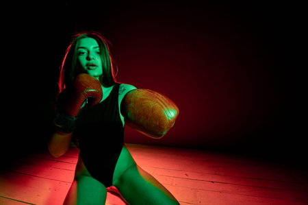 Beautiful woman with the red boxing gloves looking back and sitting on the floor. Strength and motivation. Boxing and fitness style.の写真素材