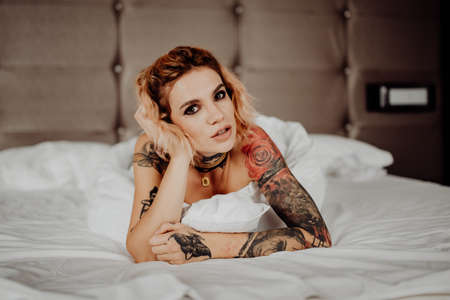 Portrait of a happy beautiful girl with tattoos. The woman is lying in bed and looking in camera.の写真素材