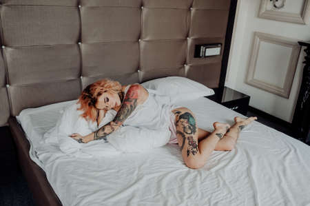 Portrait of a happy beautiful girl with tattoos. The woman is lying in bed.の写真素材