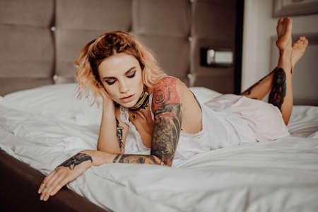 Portrait of a happy beautiful girl with tattoos. The woman is lying in bed.の写真素材