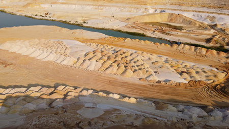 Sand quarry. Turquoise lagoon and surface mine with exposed colored minerals, equipment at the...