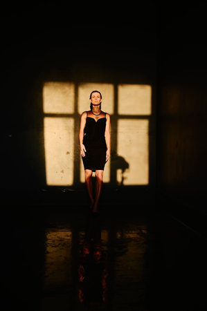 Water splash. A girl in black dress under the drops water. Wet clothes. Young woman enjoying...