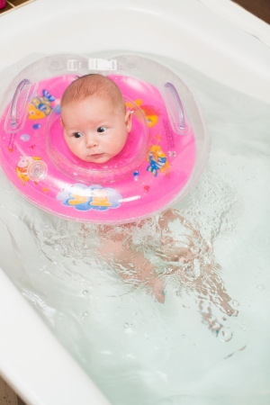 newborn baby swimming  in a bathroom with swimming around the neck. The concept of childhood and healthの写真素材