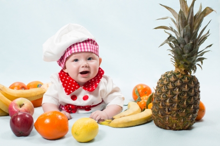 Portrait of smiling baby wearing a chef hat  surrounded by fruits. Use it for a child, healthy food conceptの写真素材