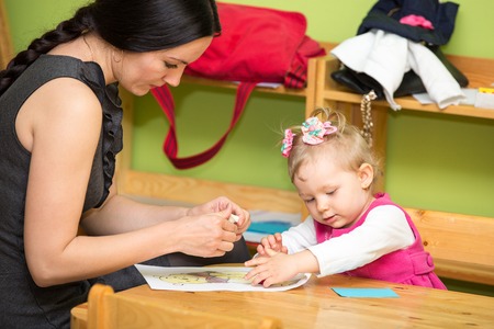 Mother and child girl drawing together with color pencils in preschool at the table in kindergartenの写真素材
