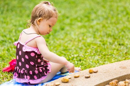 Cute little child girl in a swimsuit playing with stones on a pebble beachの写真素材