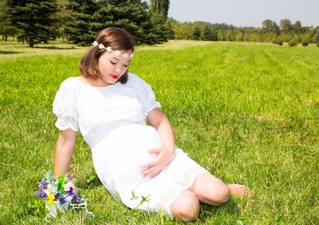 Happy asian pregnant woman with big belly rest on natureの写真素材