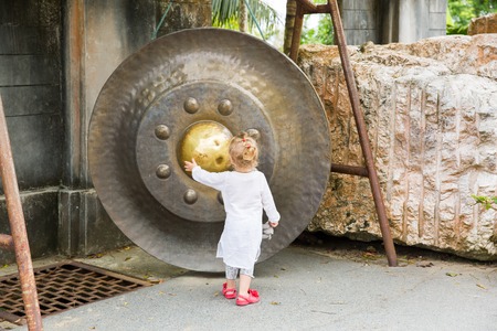 Child near Thai gong in Phuket. Tradition asian bell in Buddhism temple in Thailand. Famous Big bell wish near Gold Buddhaの写真素材