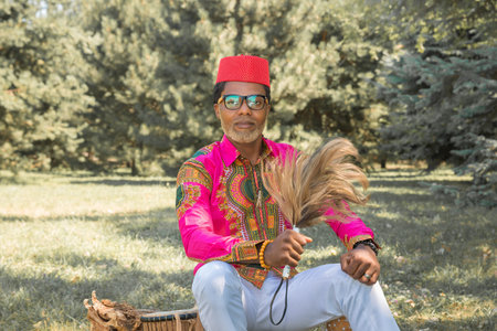 Handsome African man in a national costume plays an ethnic drum, djembe.