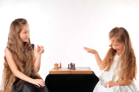 Little girls sisters play chess on white background. Sport and hobby concept. Cognitive development. Intellectual game. Smart children.の写真素材
