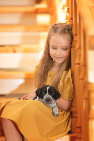 Child with a dog. Little girl plays with a with a puppy dog at home on the stairs. Kid and animal.の写真素材