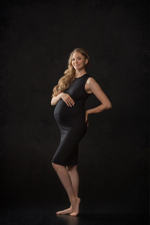 Pregnant woman on black background with big tummy, waiting for baby. Pregnancy, motherhood conceptの写真素材