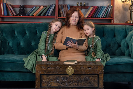 Happy grandma and grandchildren reading book together and having fun at home