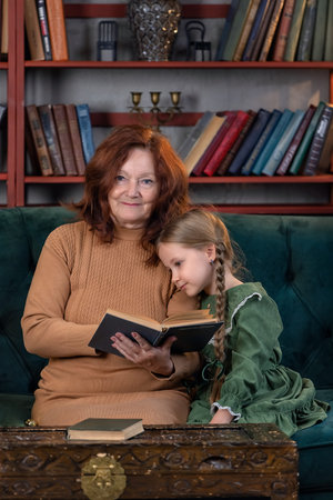 Happy grandma and granddaughter reading book together and having fun at homeの写真素材