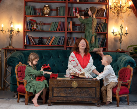 Happy grandma and grandchildren reading book together and having fun at homeの写真素材