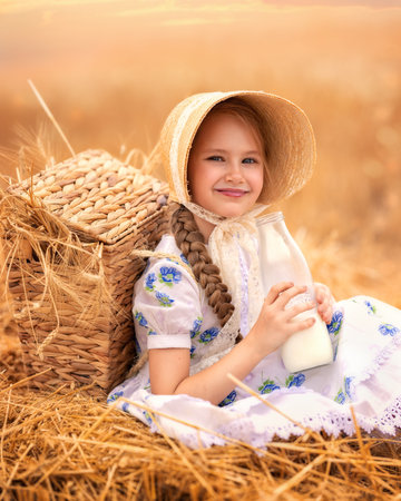 A portrait of a happy girl in a wheat field at sunset. A child holds a glass jar with milk against the background of rye ears.の写真素材