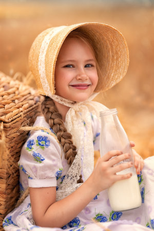 A portrait of a happy girl in a wheat field at sunset. A child holds a glass jar with milk against the background of rye ears.の写真素材