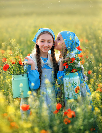 Sisters. Portrait of cute children girls in poppy field. Kids in blue dress happy with poppy bouquet at summer sunsetの写真素材