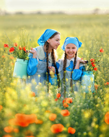 Sisters. Portrait of cute children girls in poppy field. Kids in blue dress happy with poppy bouquet at summer sunsetの写真素材
