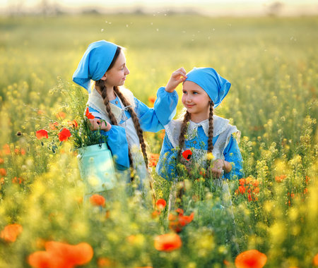 Sisters. Portrait of cute children girls in poppy field. Kids in blue dress happy with poppy bouquet at summer sunsetの写真素材