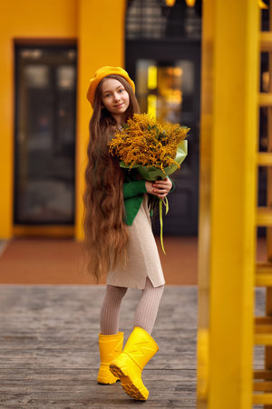 Beautiful girl kid in beret with spring yellow mimosa flowers bouquet at city street. Portrait of pretty child with long hair in park outdoors.の写真素材