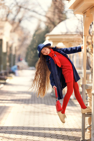 Beautiful girl kid in hat with spring yellow mimosa flowers bouquet at city street. Portrait of pretty child with long hair in park outdoors.の写真素材