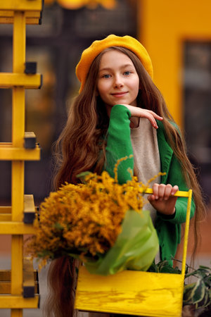 Beautiful girl kid in beret with spring yellow mimosa flowers bouquet at city street. Portrait of pretty child with long hair in park outdoors.の写真素材