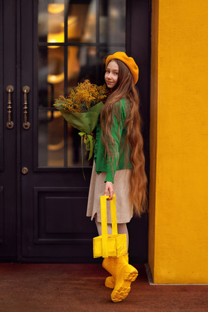 Beautiful girl kid in beret with spring yellow mimosa flowers bouquet at city street. Portrait of pretty child with long hair in park outdoors.の写真素材