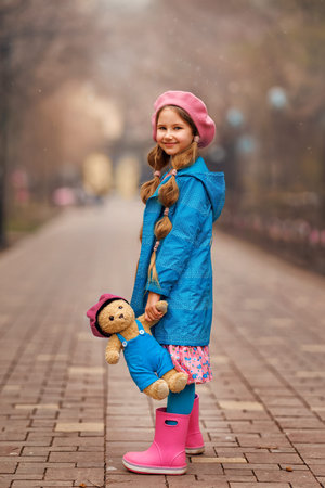 Beautiful girl kid with teddy bear at city street. Portrait of pretty child in park outdoors.の写真素材