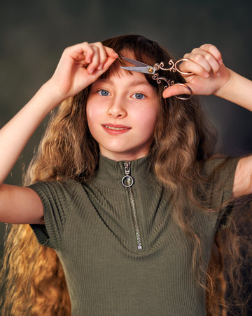 Portrait of a emotional beautiful girl kid with scissors isolated on black background. Teen girl in...