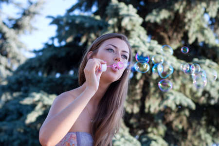 young woman makes soap bubbles sitting on a bench in parkの写真素材