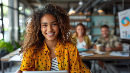 A woman with curly hair smiles at the camera during a meeting in a modern office setting.の素材