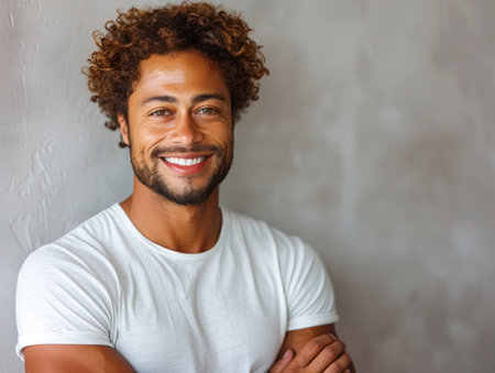 A portrait of a man with curly brown hair smiling against a gray wall.の素材