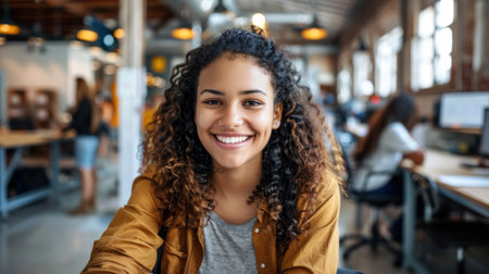A young woman with curly hair smiles brightly in a modern office setting.の素材