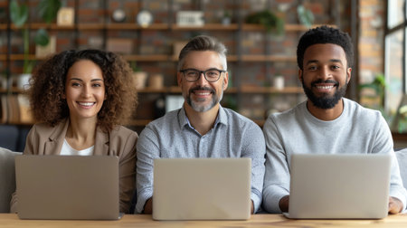 A diverse group of three professionals, a woman, a man, and a man, working on laptops in a modern office setting.の素材