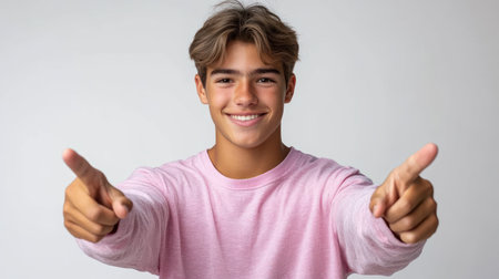 A cheerful young man in a pink long sleeve shirt poses playfully with finger guns.の素材