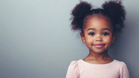 A cheerful young girl with curly hair stands smiling in a light gray studio, showing her playful spirit.の素材
