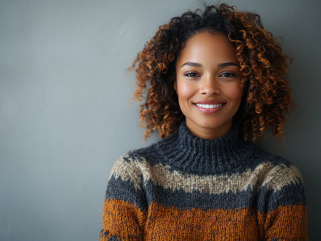 Woman with curly hair smiles warmly while wearing a stylish sweater in a calming indoor setting.の素材